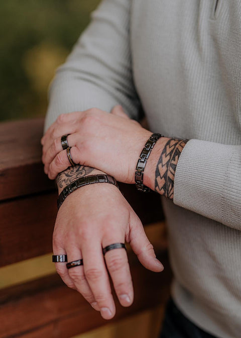 3. Close-up of man's hands wearing Leomani Trey black ceramic bracelet and rings, resting on wooden railing