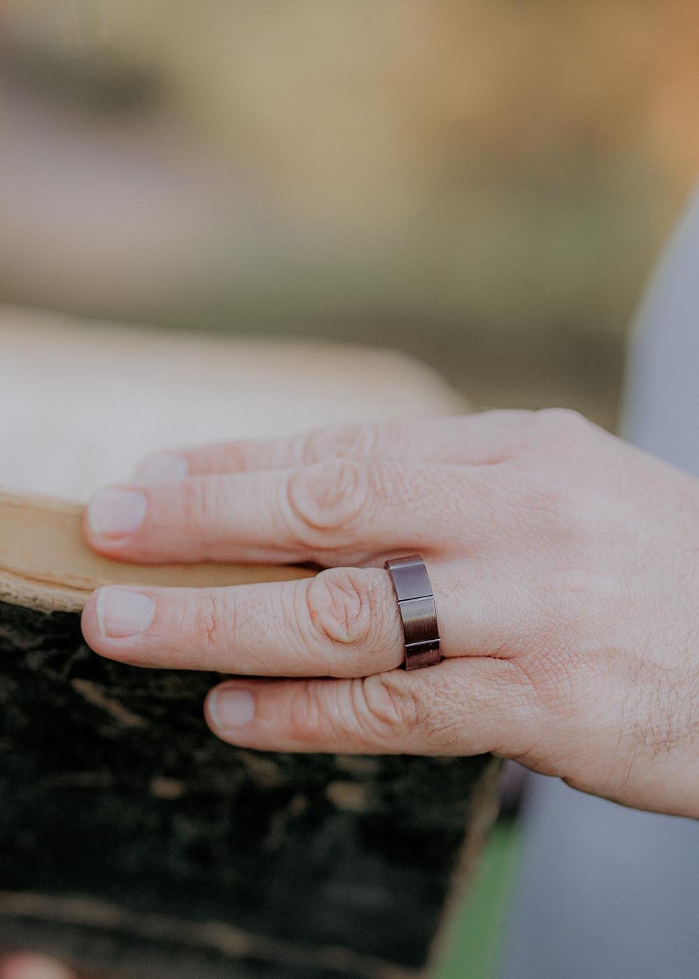 1. Man wearing Leomani brown ceramic ring on finger while holding a wooden object outdoors