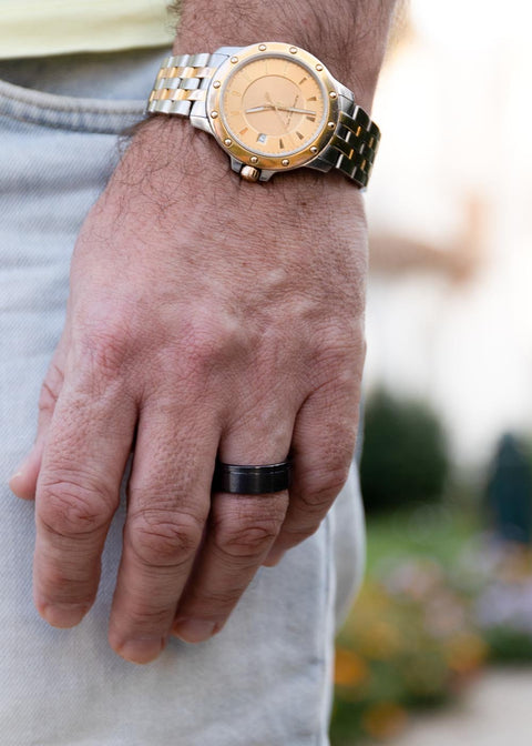 1. Man wearing Leomani black ceramic ring Lion on left hand with gold watch, casual outdoor setting