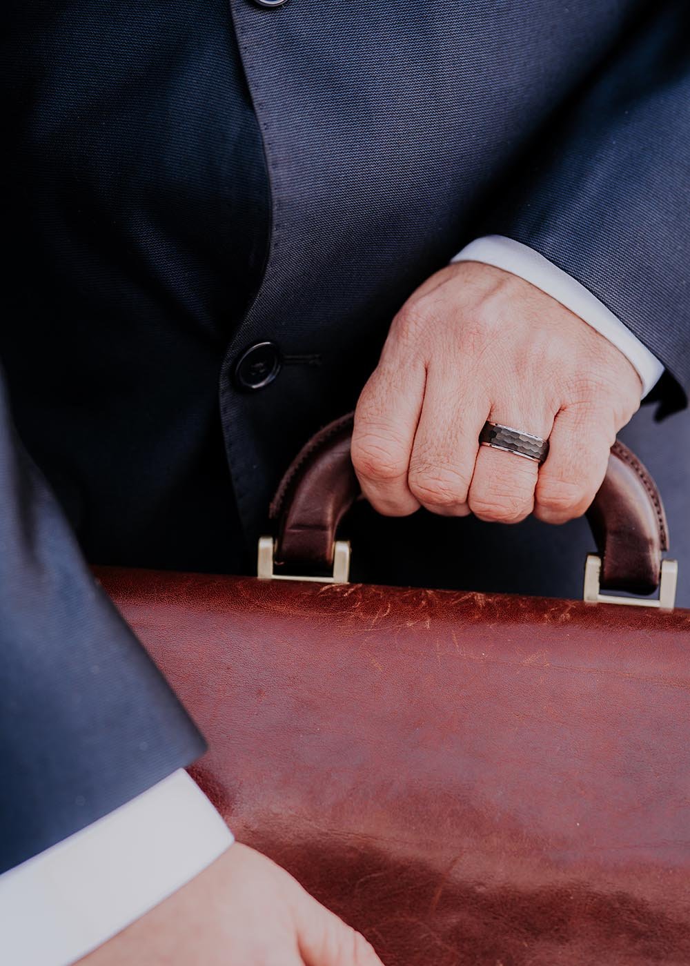 1. Man wearing Leomani men's tungsten ring Lejon while holding a leather briefcase, showcasing the ring's durability and sophistication in a business setting