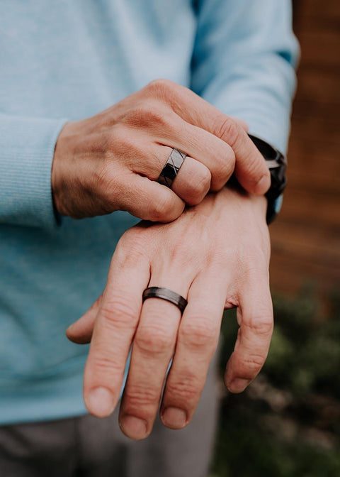 1. Two men's hands wearing black ceramic rings by Leomani, one hand adjusting a watch, in an outdoor setting