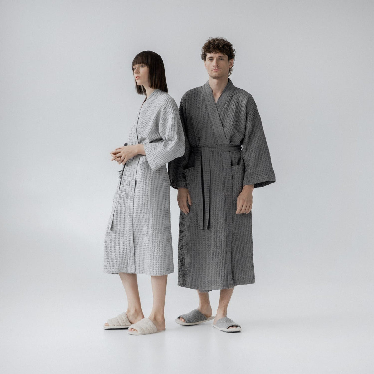 4. Man and woman wearing light grey and dark grey bathrobes standing side by side in studio