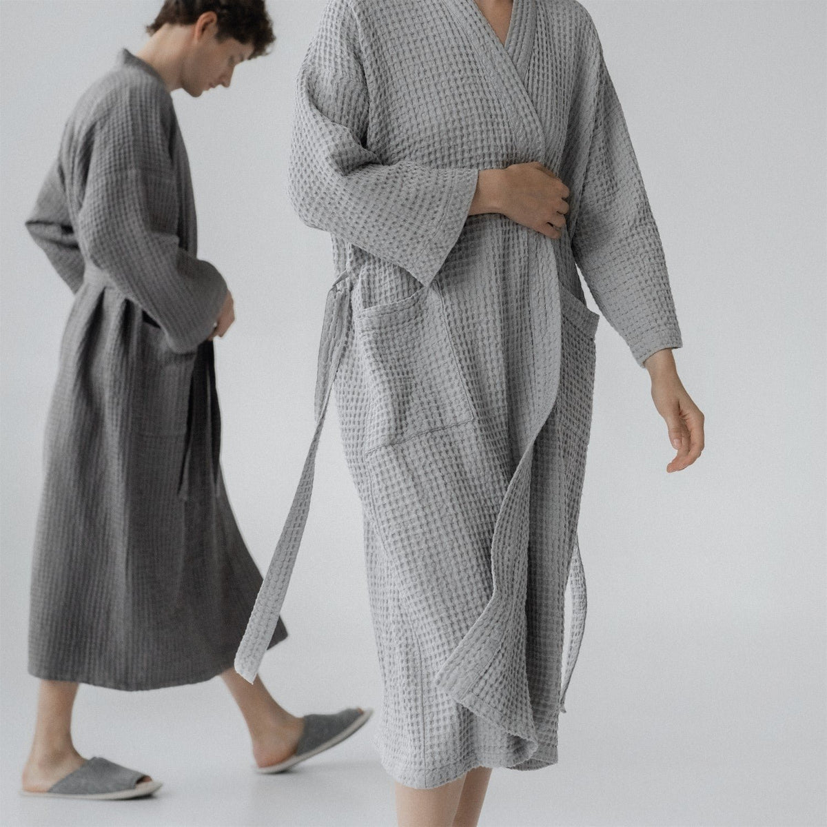1. Man and woman wearing light grey and dark grey honeycomb waffle bathrobes in a minimalist setting