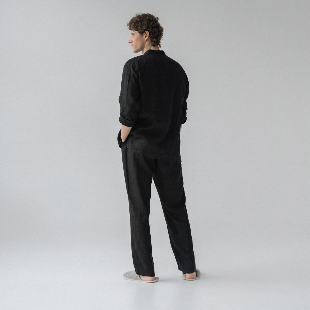 3. Man shown from back wearing black linen loungewear set with hands in pockets in a studio setting