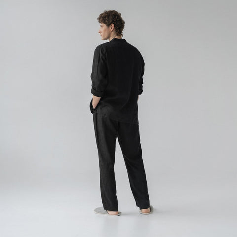 3. Man shown from back wearing black linen loungewear set with hands in pockets in a studio setting