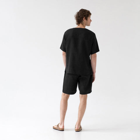 2. Back view of man in black linen pyjama set with relaxed fit, in a studio setting
