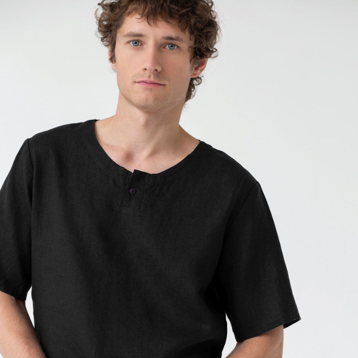 4. Close-up of man wearing black linen pyjama top with wide round neck and button fastening