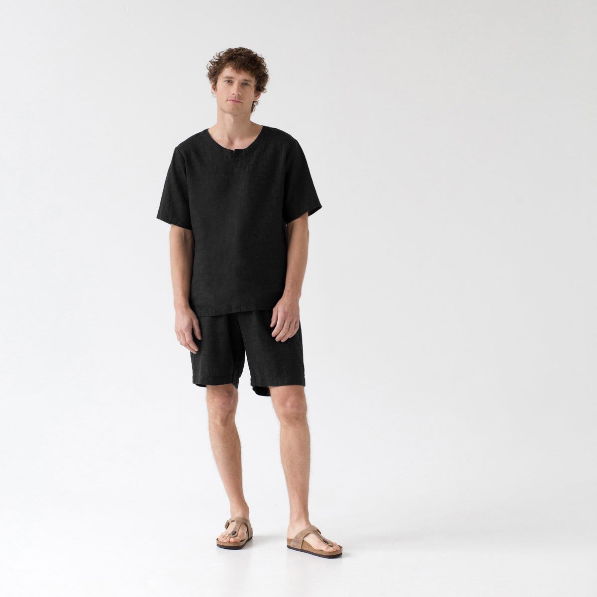 1. Man wearing black linen pyjama set with short sleeves and shorts, standing in a studio setting