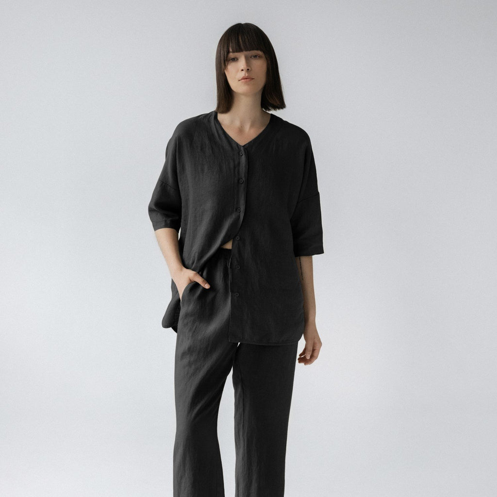 2. Woman in black linen loungewear set with buttoned V-neck top and elasticated waistband trousers, standing front-facing on a plain background