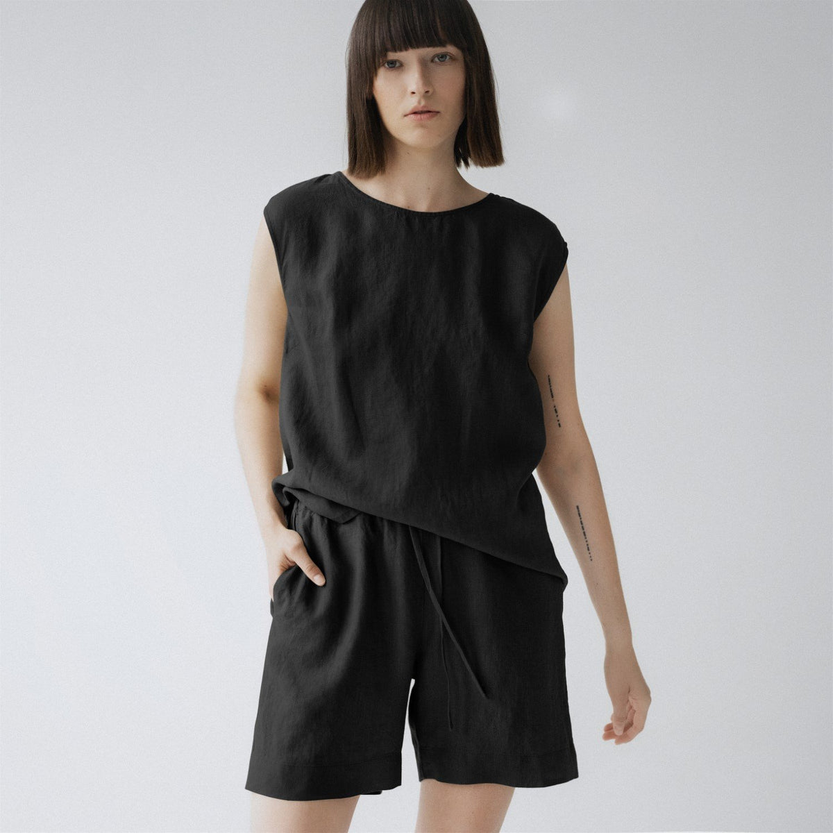 1. Woman wearing black sleeveless linen pyjama set with relaxed fit shorts, standing in a studio setting