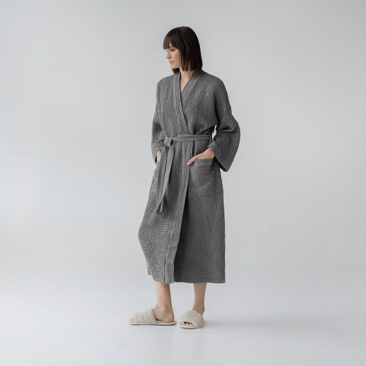 9. Woman wearing dark grey honeycomb waffle bathrobe with hands in pockets in studio