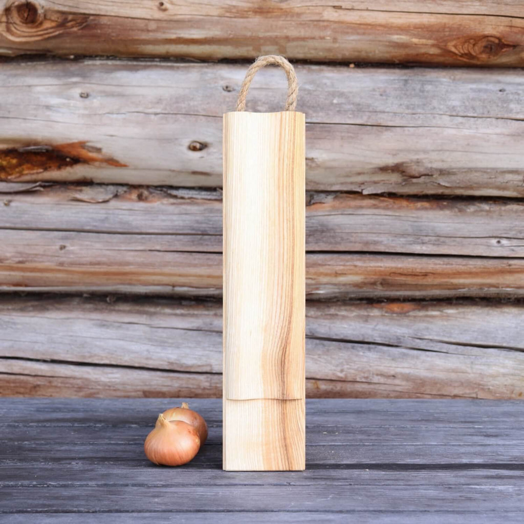 1. Wooden cutting board with rope handle standing upright on rustic wooden surface with onions, against a wooden wall background