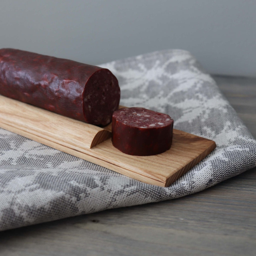 2. Wooden cutting board with a whole and sliced sausage on a patterned cloth, showcasing the board's groove design