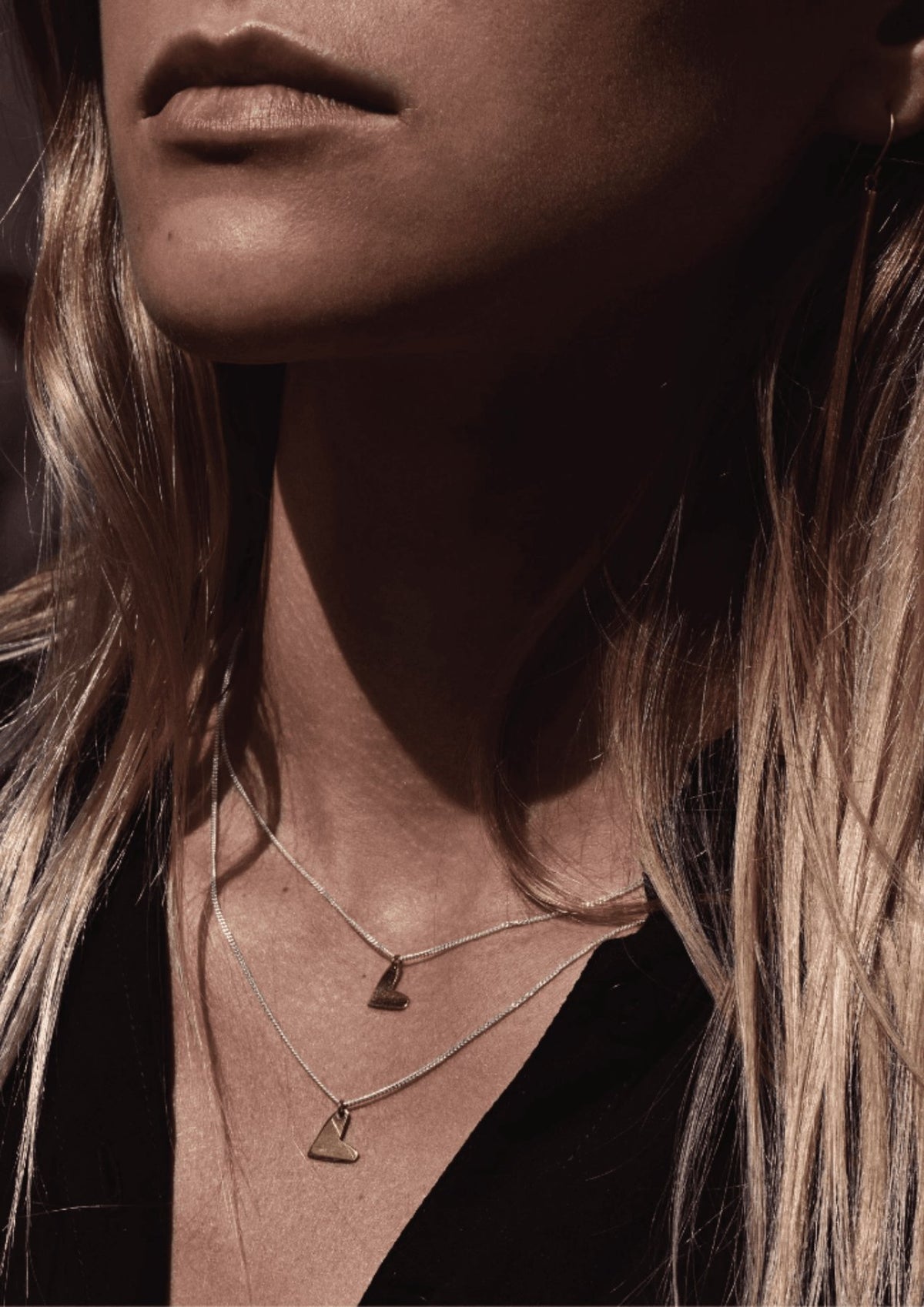 8. Women's Love Necklace in gold by NO MORE, layered with another necklace, worn with a black top