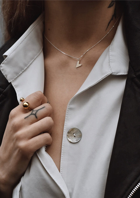 1. Woman wearing NO MORE Love Necklace in silver with heart pendant, styled with a white shirt and black jacket