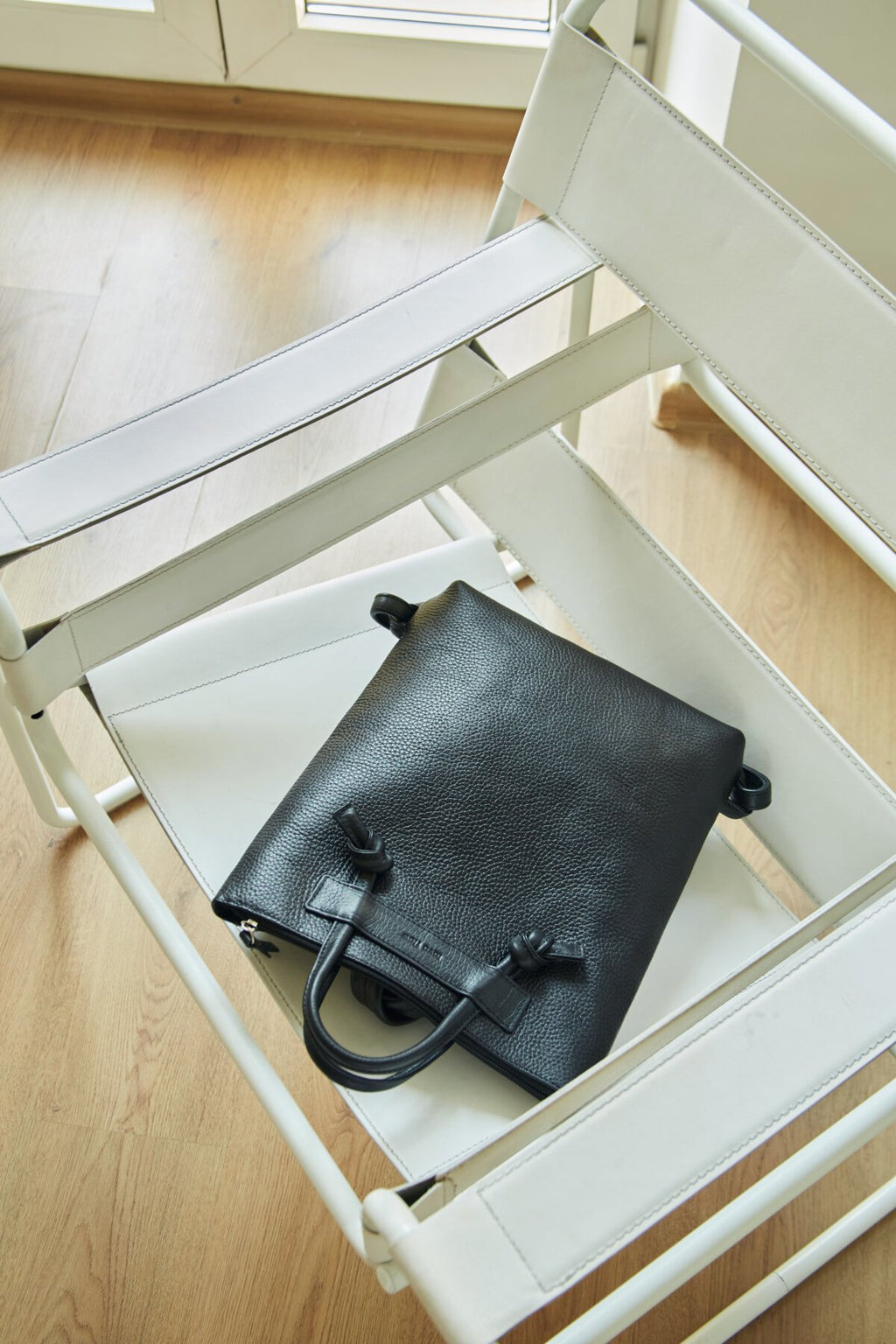 3. Lava Flow ALICE ARM black leather backpack on white chair, showing minimalist design and texture