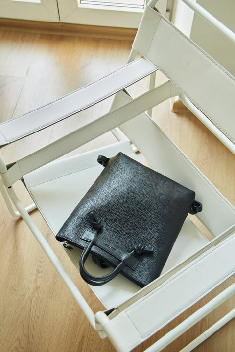 3. Lava Flow ALICE ARM black leather backpack on white chair, showing minimalist design and texture