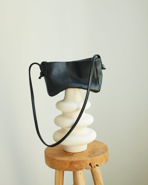 4. Lava Flow Crossbody Bag MERU in black displayed on a decorative stand, showing adjustable strap and design