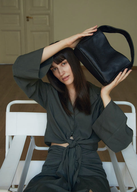 2. Woman sitting with Lava Flow Crossbody Bag MERU in black, highlighting versatile style and craftsmanship