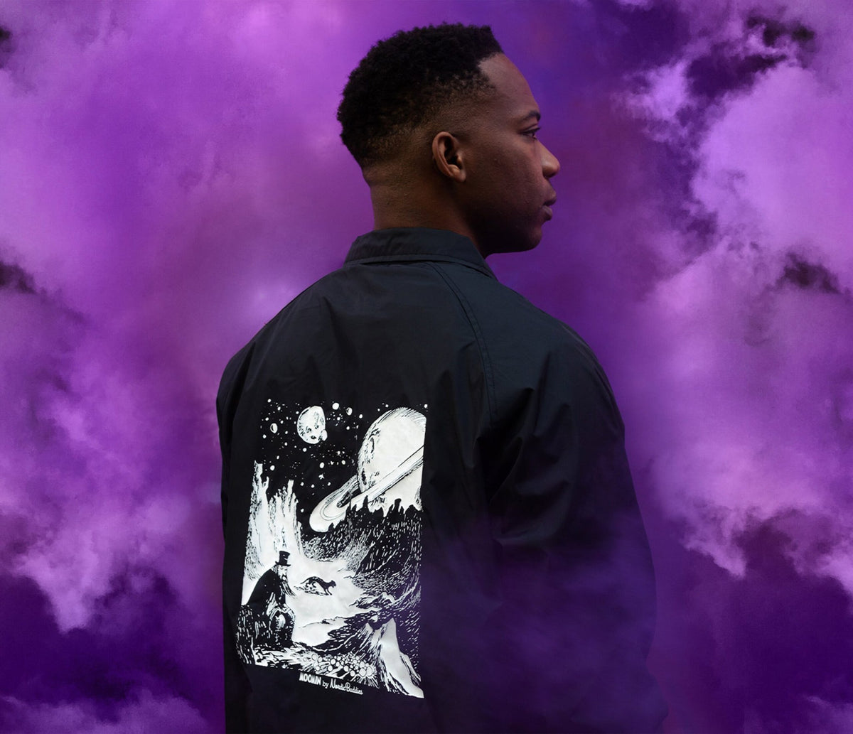 2. Unisex black Coach Jacket The Hobgoblin by Moomin shown from back on male model with purple background