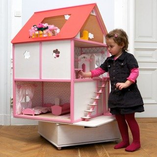 1. Young girl playing with pink and white dollhouse with red roof, featuring floral wallpaper and staircase, in a room setting
