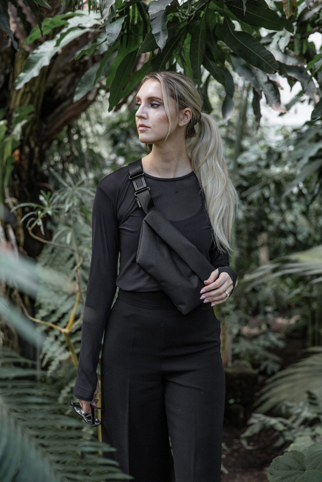 2. Woman wearing Nordhale OSLO Cross Body Bag in black, styled with black outfit, in lush garden setting
