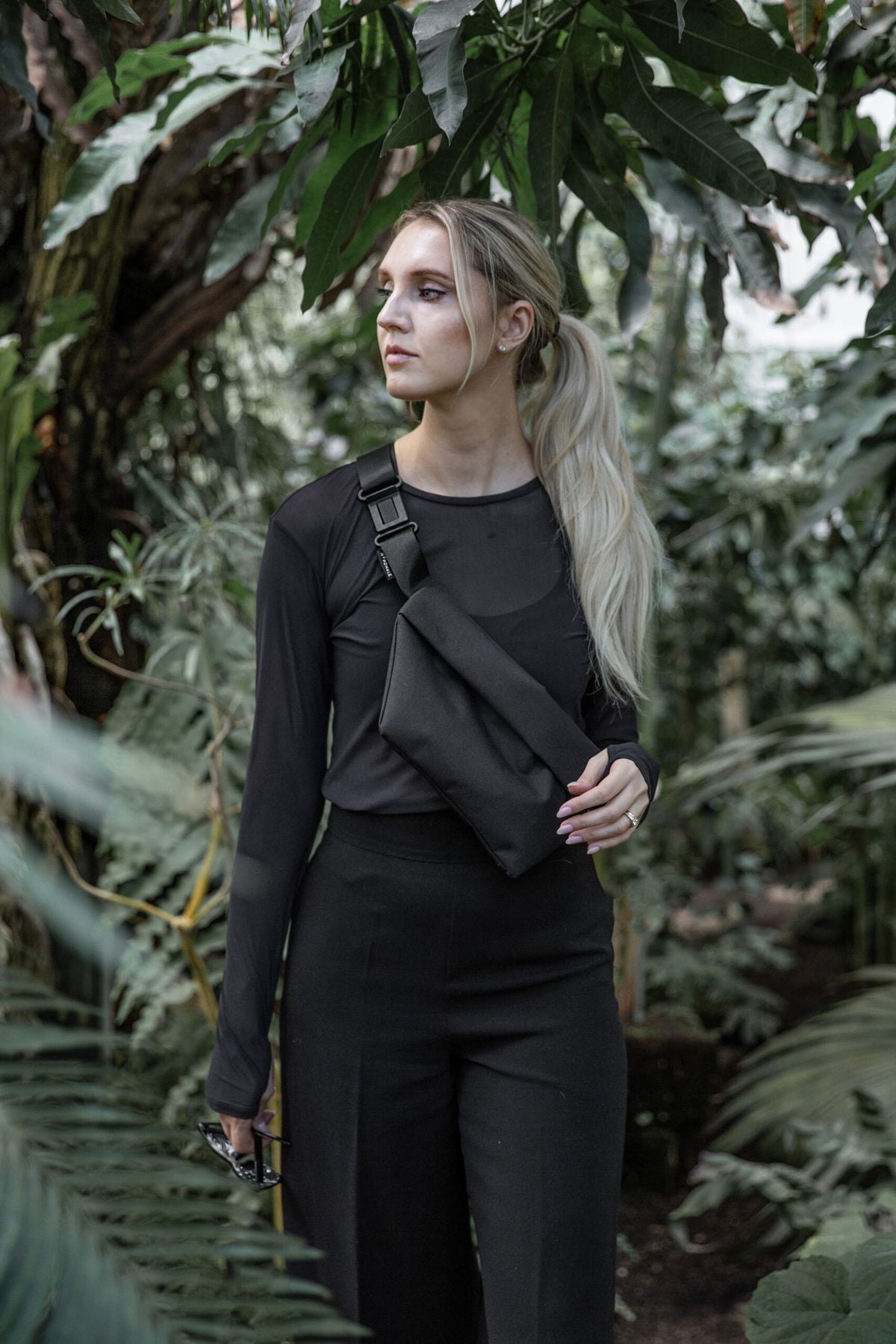 2. Woman wearing Nordhale OSLO Cross Body Bag in black, styled with black outfit, in lush garden setting