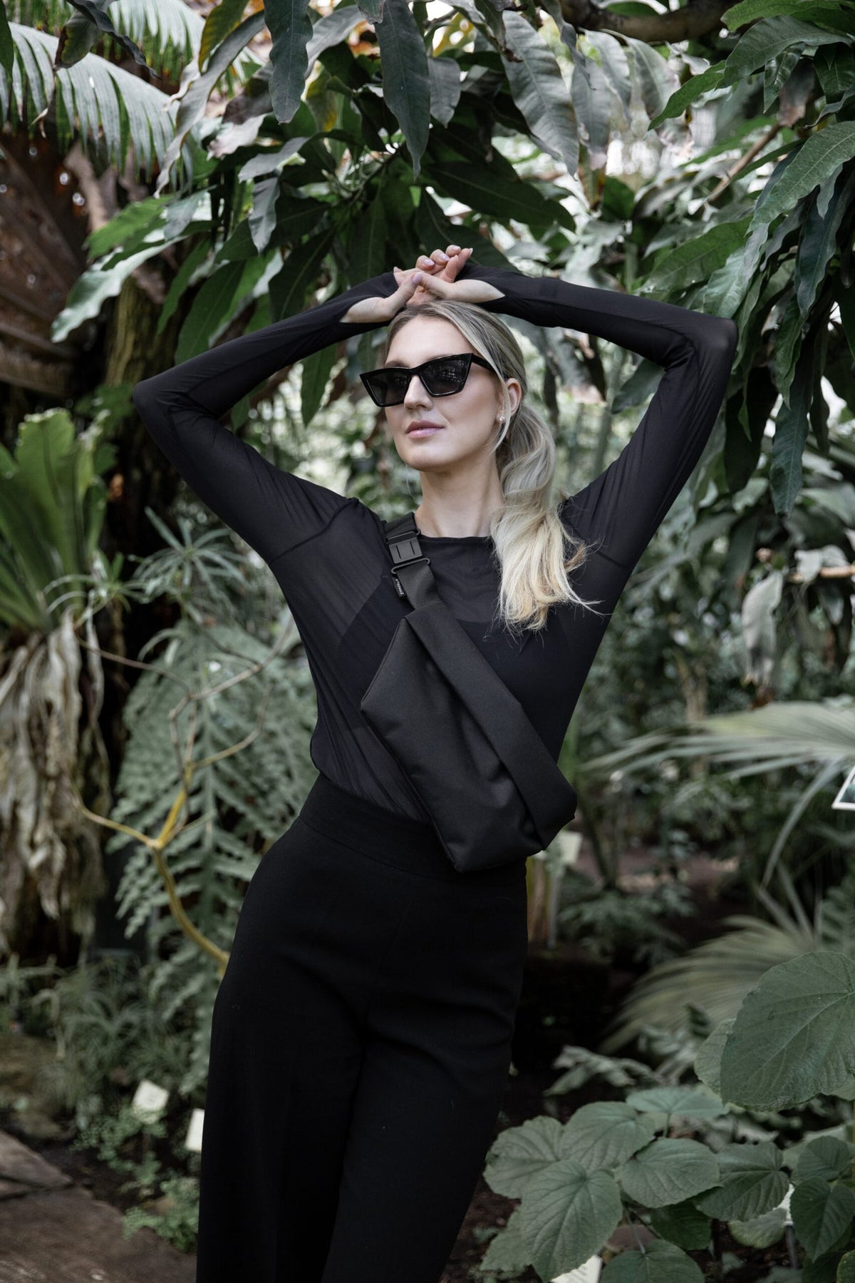 1. Woman wearing Nordhale OSLO Cross Body Bag in black, styled over white hoodie, shown from back in lifestyle setting