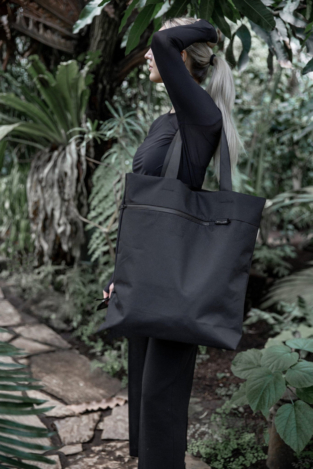 8. Woman carrying Nordhale VIK Tote Bag in black, demonstrating its practicality and elegance in a garden setting