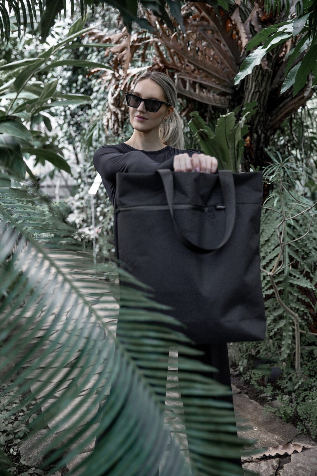 10. Woman holding Nordhale VIK Tote Bag in black, highlighting its versatility and modern design in a lush environment