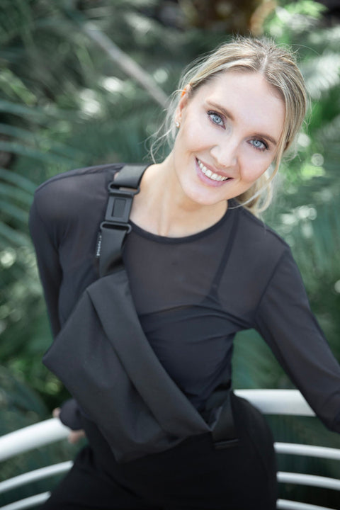 3. Woman smiling while wearing Nordhale OSLO Cross Body Bag in black, styled with black top, in outdoor setting