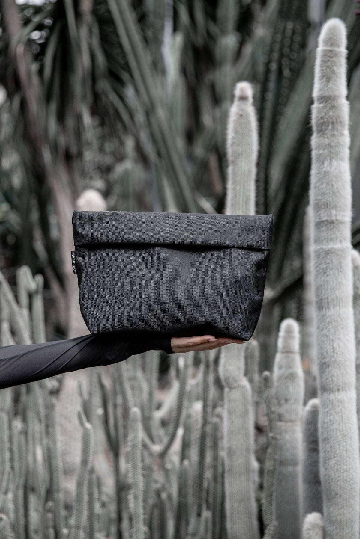 1. Nordhale NES Toiletry Bag in black held against a cactus background, showcasing minimalist design