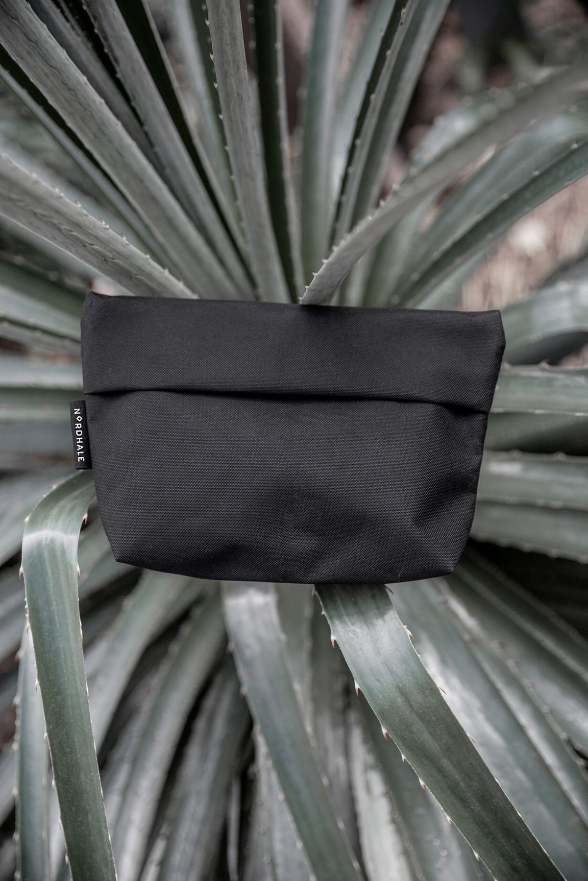 9. Nordhale NES Toiletry Bag in black on large leaf, emphasizing water-repellent fabric