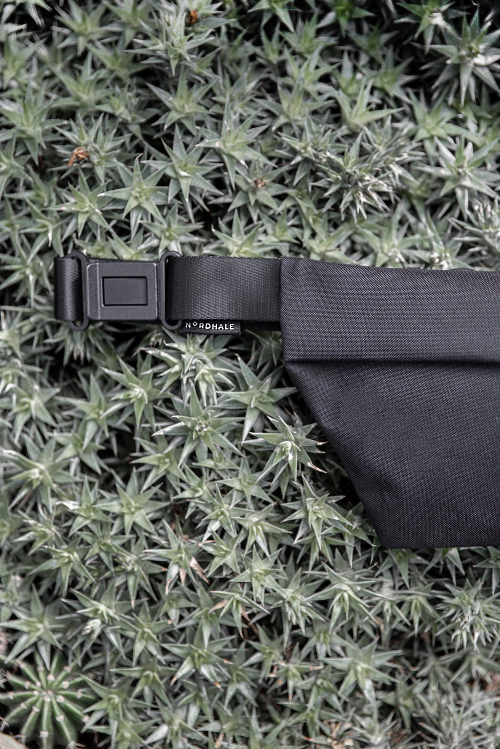 6. Nordhale OSLO Cross Body Bag in black, laid on greenery, highlighting strap and buckle