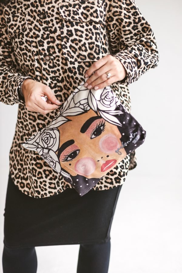 2. Garbanota YOKO makeup bag in black with illustrated face design, shown with leopard print outfit