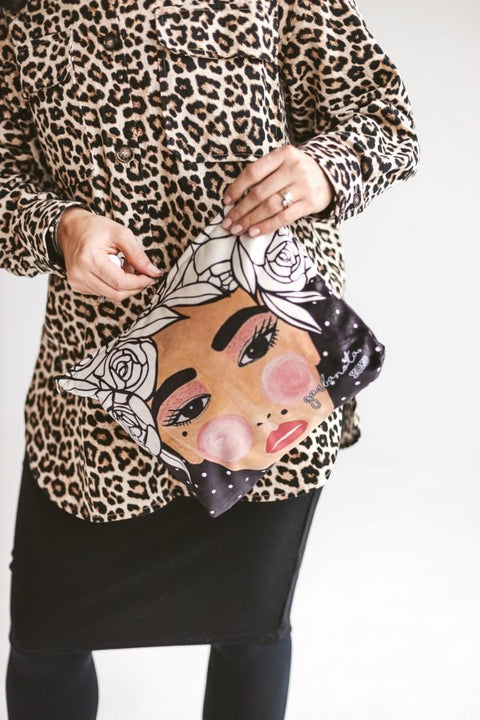 2. Garbanota YOKO makeup bag in black with illustrated face design, shown with leopard print outfit