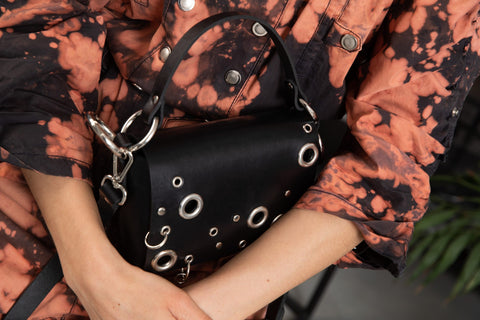 3. Close-up of PYKOK Handbag Mia in black studded leather, held by woman in orange jacket