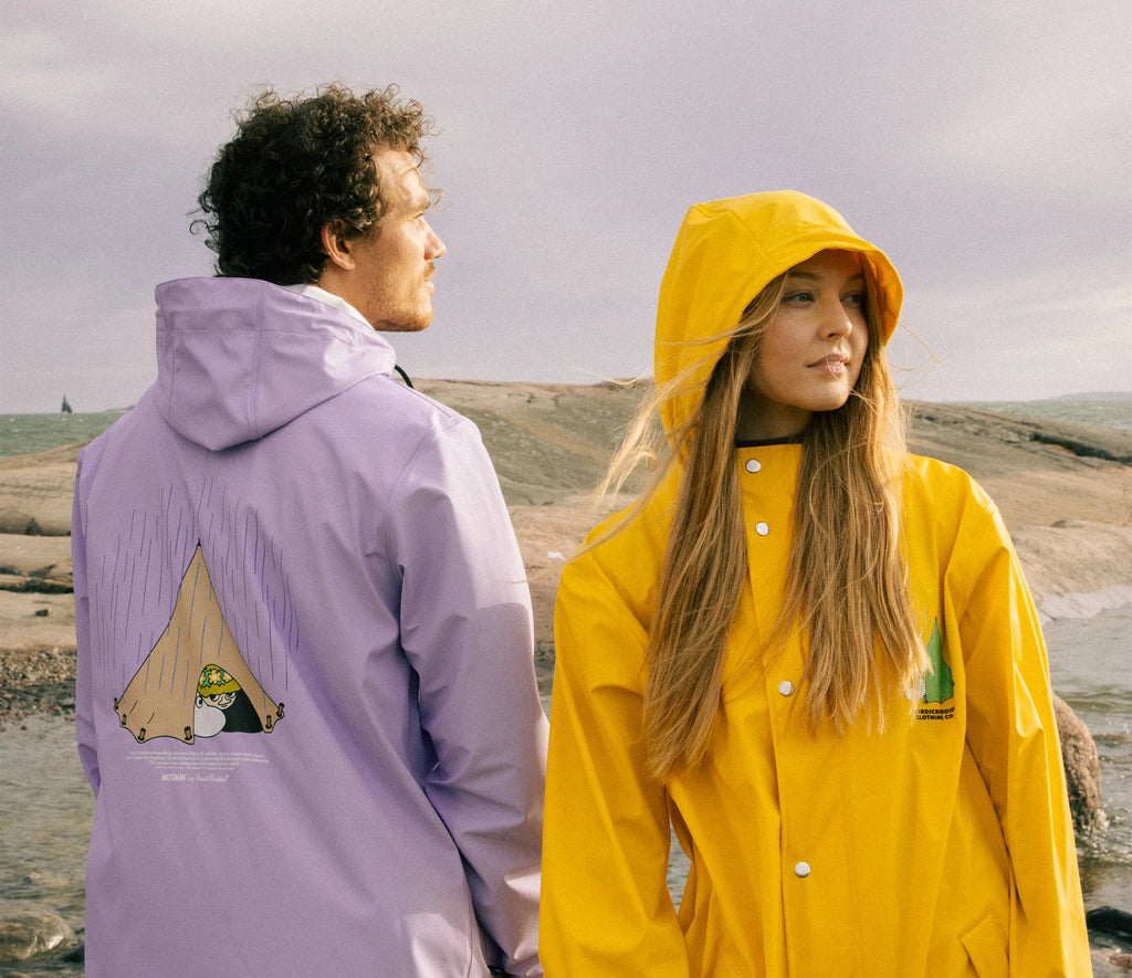 1. Unisex yellow Moomin Adventure Rain Jacket worn by male and female models on rocky terrain