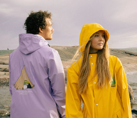 1. Unisex yellow Moomin Adventure Rain Jacket worn by male and female models on rocky terrain