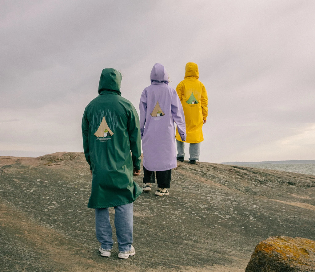 2. Unisex Moomin Adventure Rain Jacket in lilac, green, and yellow worn by three models walking on rocks