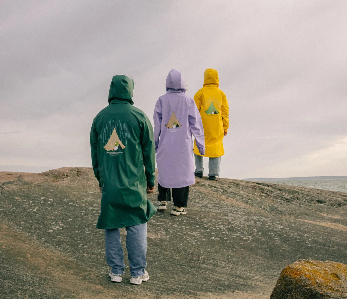 2. Unisex Moomin Adventure Rain Jacket in lilac, green, and yellow worn by three models walking on rocks