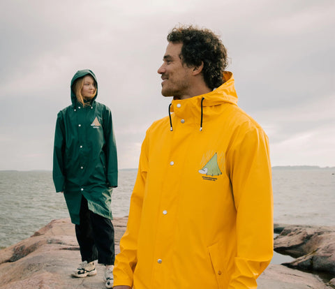 2. Unisex yellow Moomin Adventure Rain Jacket worn by male model, with female model in green jacket in background