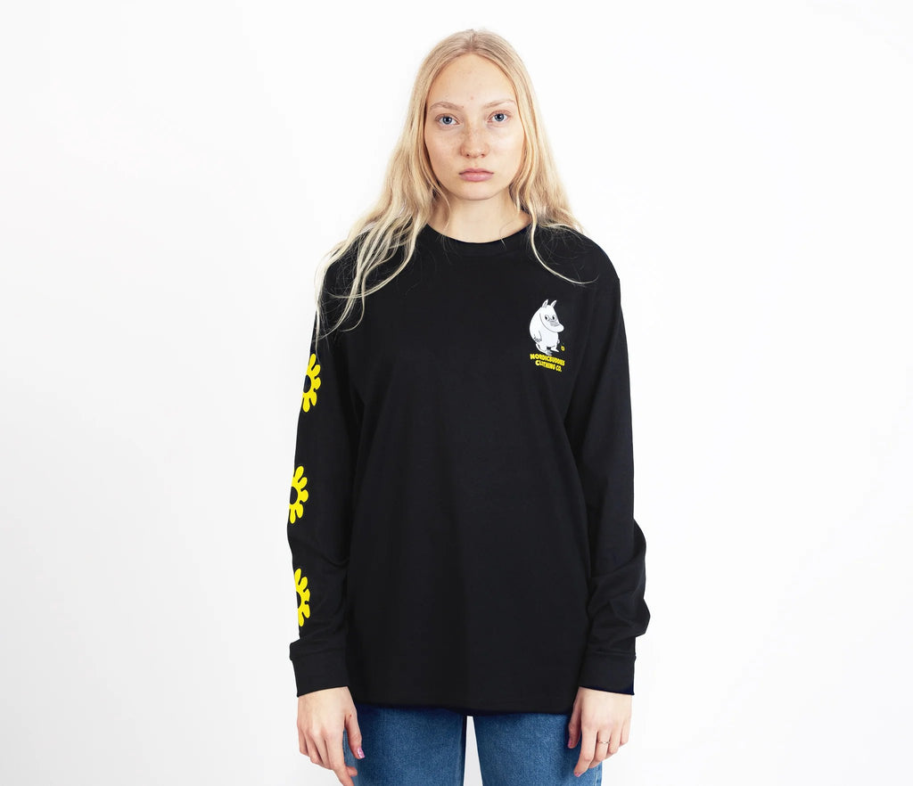 8. Unisex black Moomintroll's Flower longsleeve shirt worn by female model, featuring yellow floral sleeve design and Moomin logo, studio setting