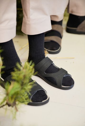 1. Lifestyle image of Omaking black professional heel-cushioned sandals worn with socks, showcasing adjustable Velcro straps and ergonomic design