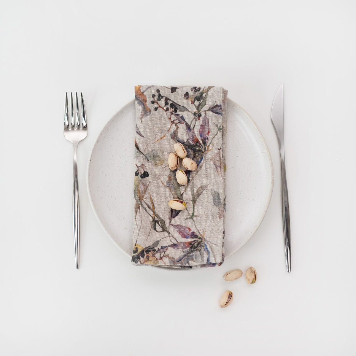 4. Floral linen napkin on a white plate with pistachios, accompanied by fork and knife