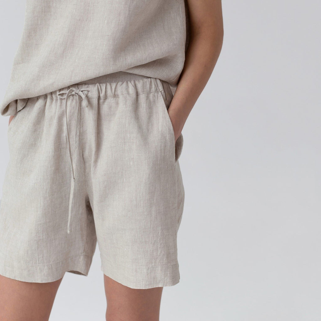 3. Close-up of beige linen pyjama shorts with elasticated waistband and drawstring, hand in pocket