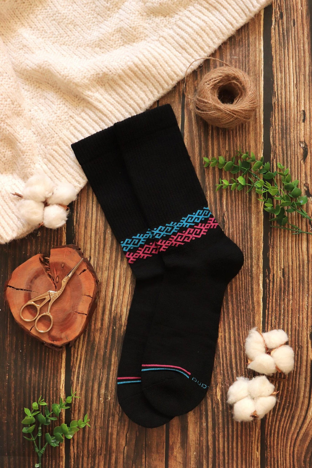 1. Flat lay of Baltland unisex black athletic cushioned Merino wool socks with colorful geometric pattern, styled on wooden surface