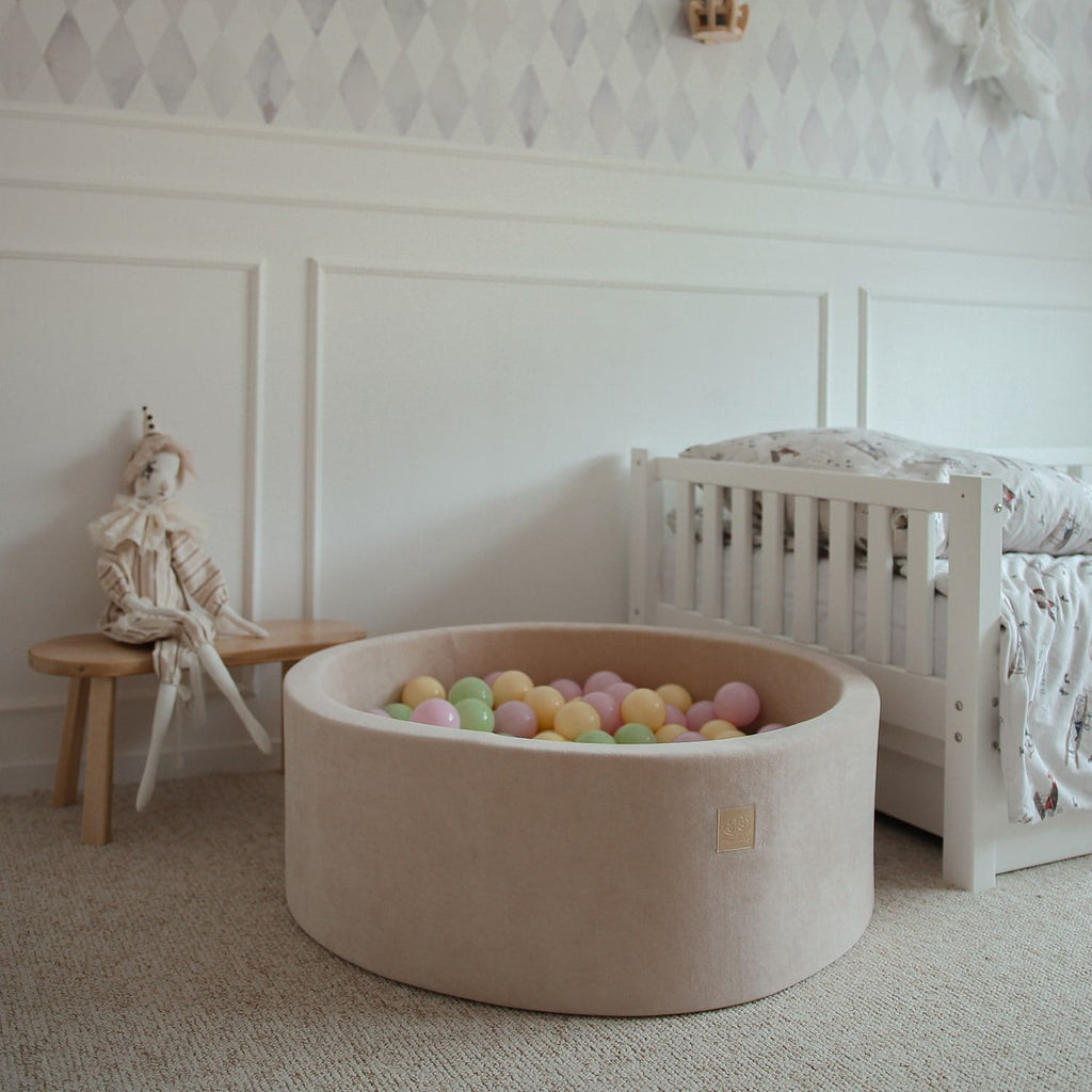 4. Beige MeowBaby foam ball pit with pastel balls next to a white bed in a child's room
