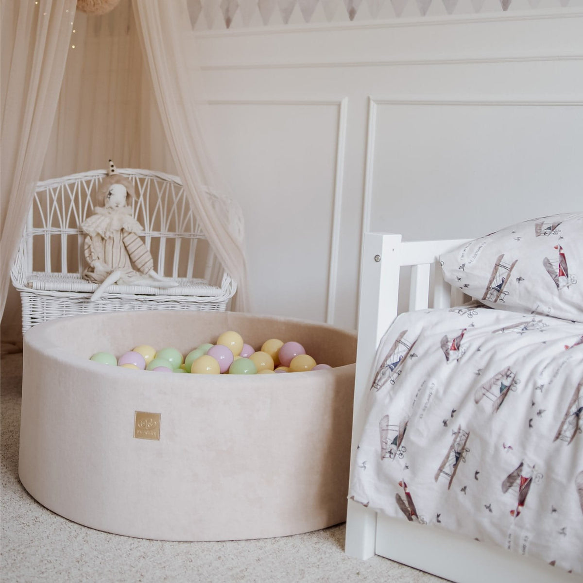 5. Beige MeowBaby foam ball pit with pastel balls beside a white wicker chair in a nursery