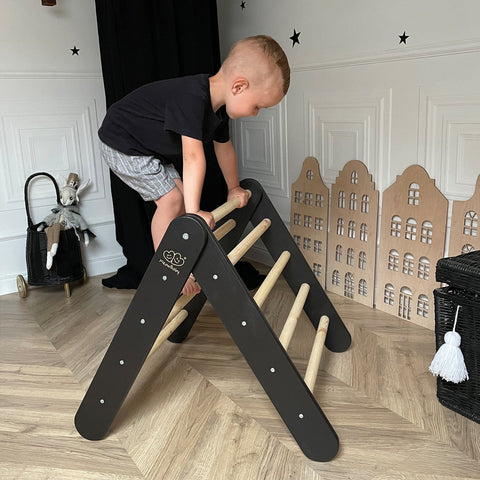 1. Child climbing on wooden Pikler ladder with black sides in a playroom setting